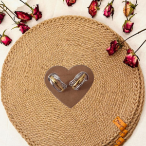Pendientes de plata con bandas doradas sobre un corazón en una base de esparto y rosas secas